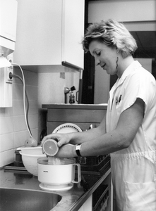 826703 Afbeelding van een verpleegkundige die bezig is met het uitpersen van sinaasappels in een keukentje op een ...